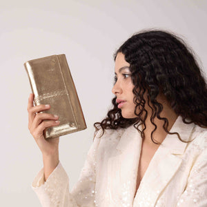 Woman holding a gold clutch against a plain background