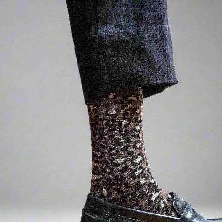 Person wearing leopard print socks with a black leather shoe on a neutral background
