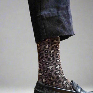 Person wearing leopard print socks with a black leather shoe on a neutral background